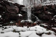 Şelale ve kar ile çevrili doğa manzarası, huzurlu ve serinlatıcı bir ortam.